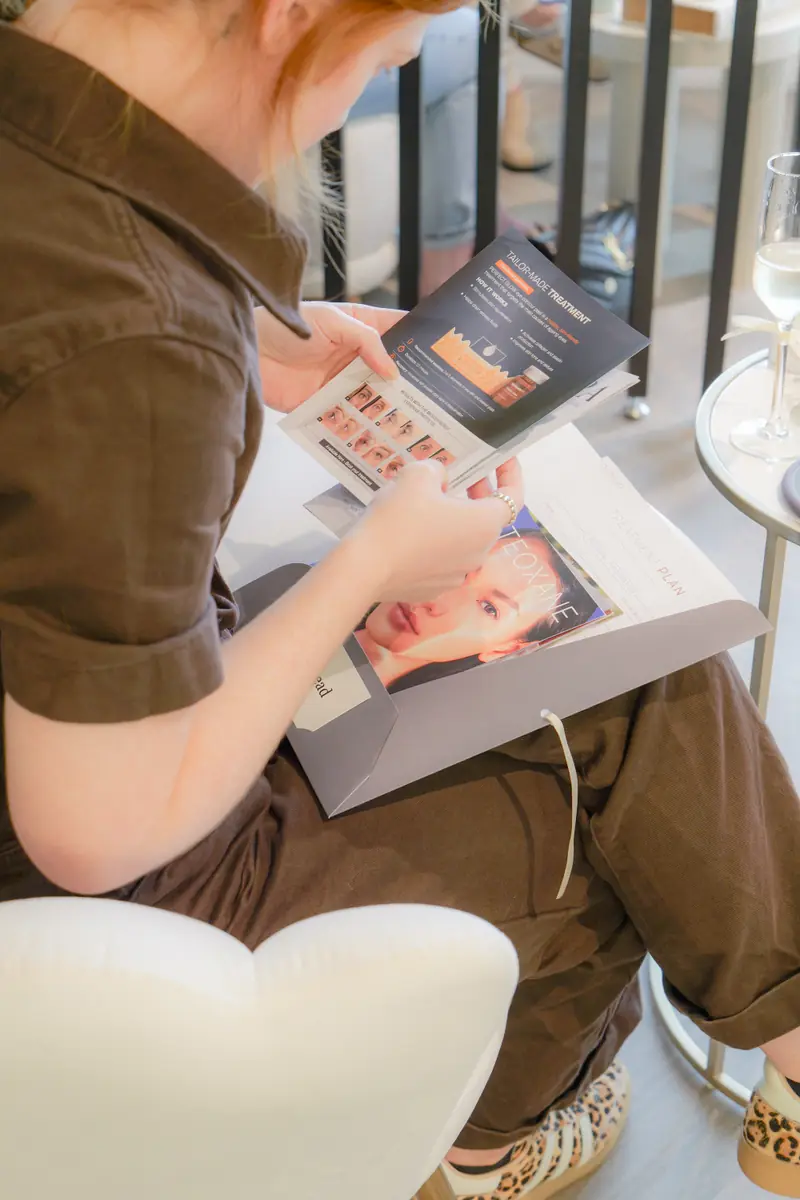 A guest reading a treatment brochure from her take-home folder, with a glass of prosecco beside her.