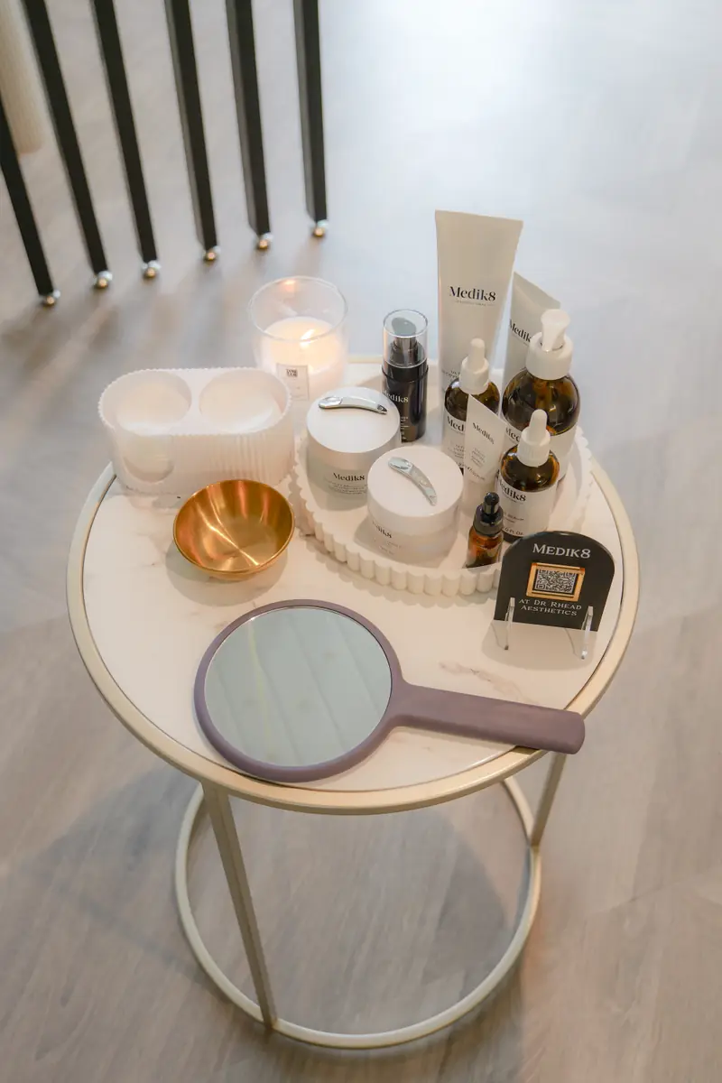 Medik8 serums, creams and cleansers arranged on a marble table with a copper bowl, candle and hand mirror.