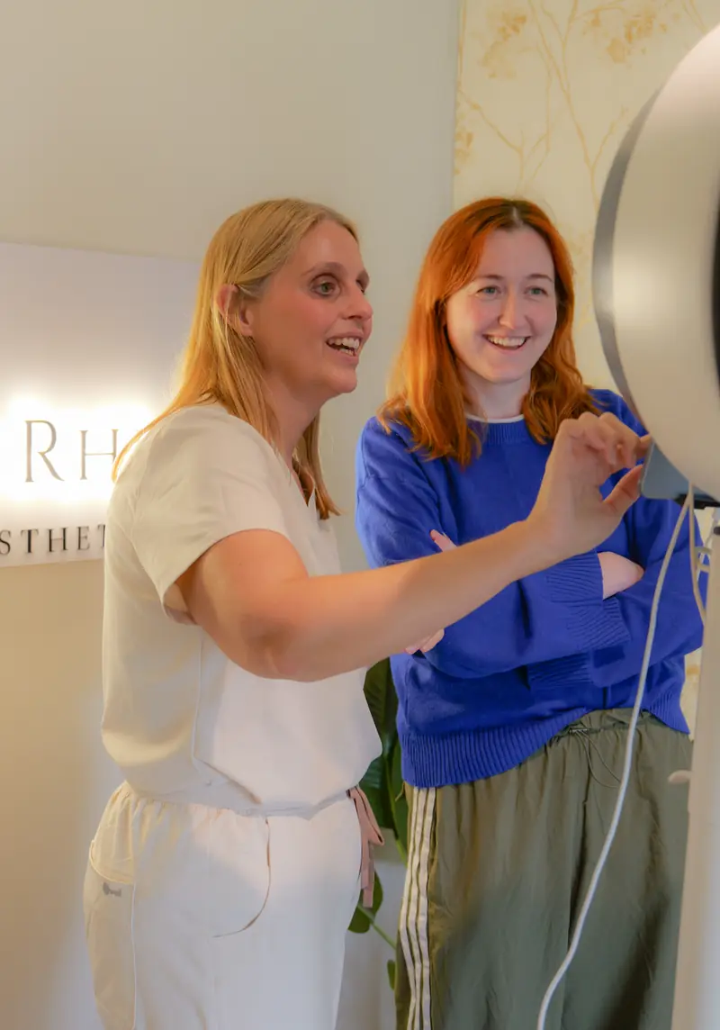 A member of the Dr Rhead Aesthetics team explaining the Observ skin analysis scanner to a smiling guest.