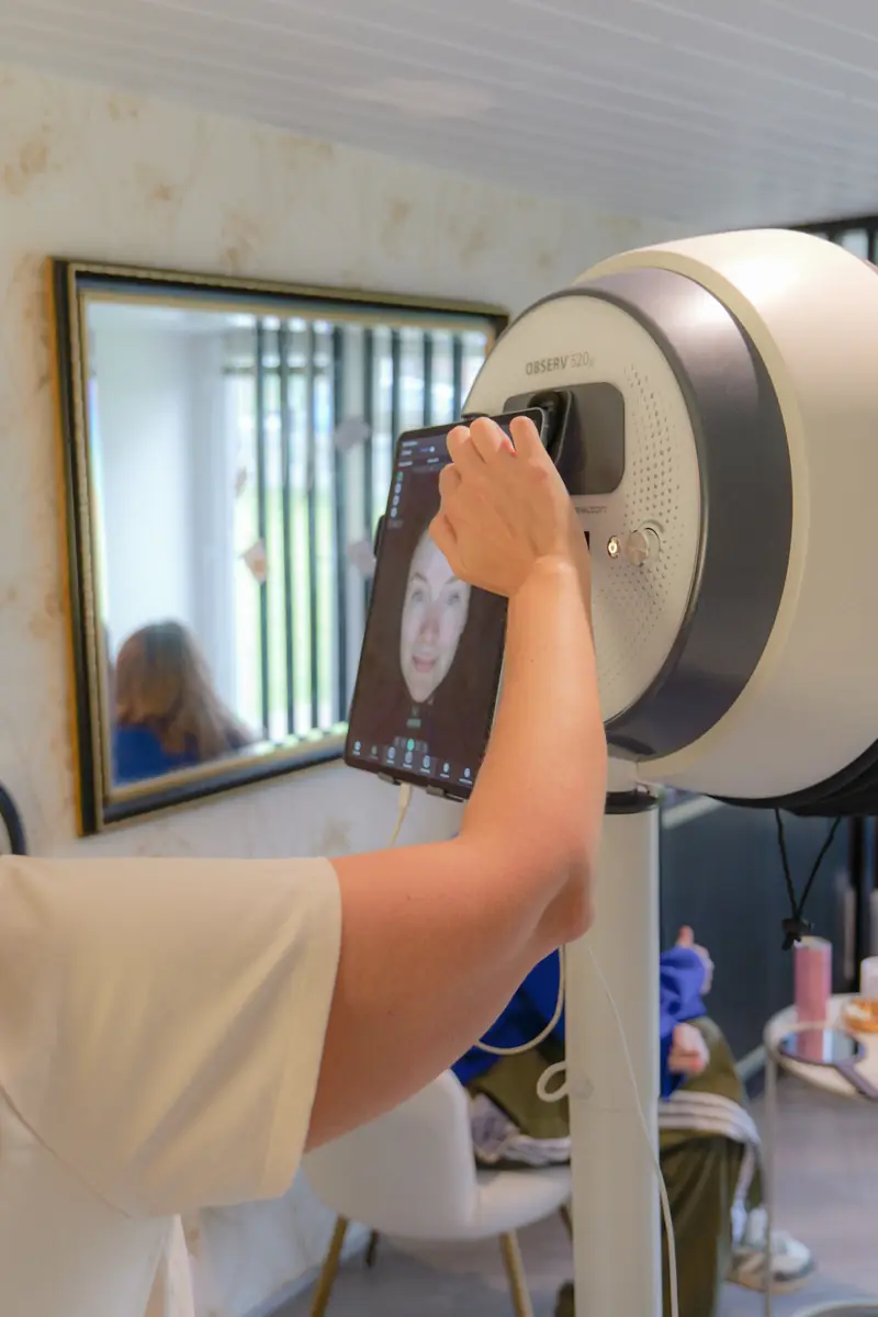 A team member holding the tablet against the Observ skin analysis scanner while a guest's face scan appears on screen.