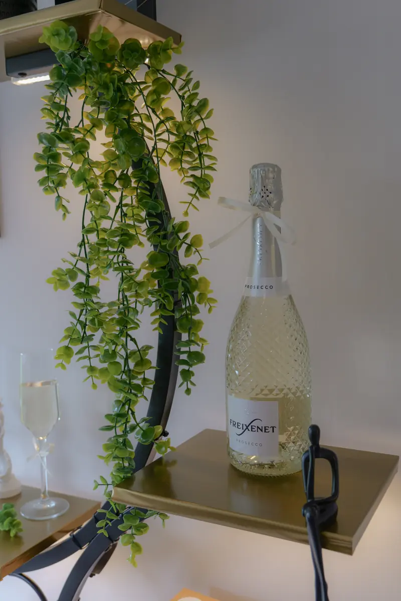 A bottle of prosecco tied with ribbon on a gold shelf, ready to pour for guests at The Signature Event.
