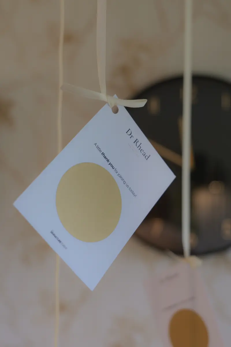 A Dr Rhead thank-you tag with a gold scratch card, hanging from a ribbon at The Signature Event.