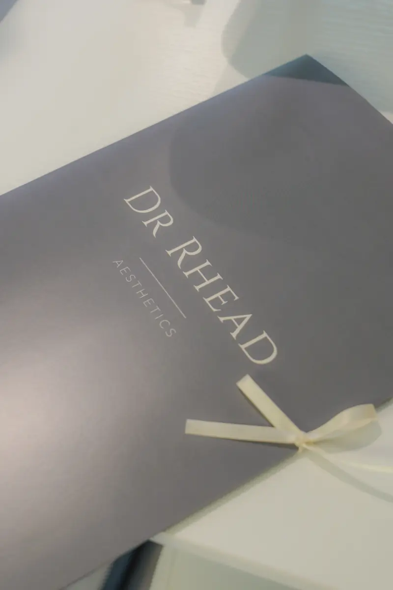 A grey Dr Rhead Aesthetics take-home folder tied with a cream ribbon.
